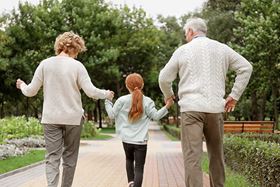 An elderly couple walking away from the viewer while holding hands with their granddaughter who is between them
