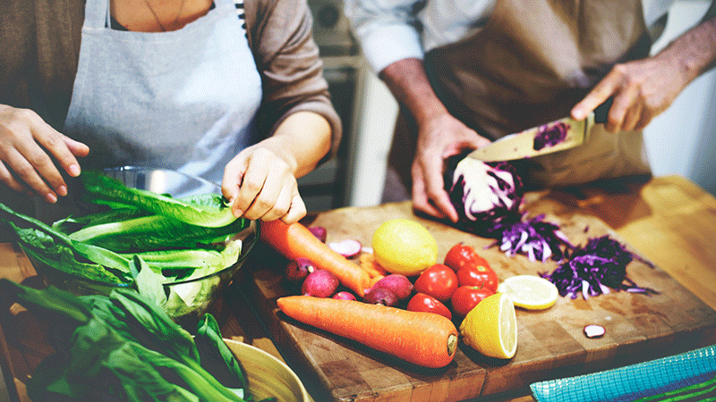 Pareja picando verduras sobre una tabla de cortar