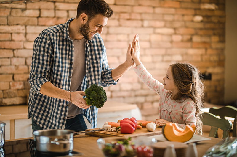 Un padre sosteniendo brócoli y chocándola con su hija