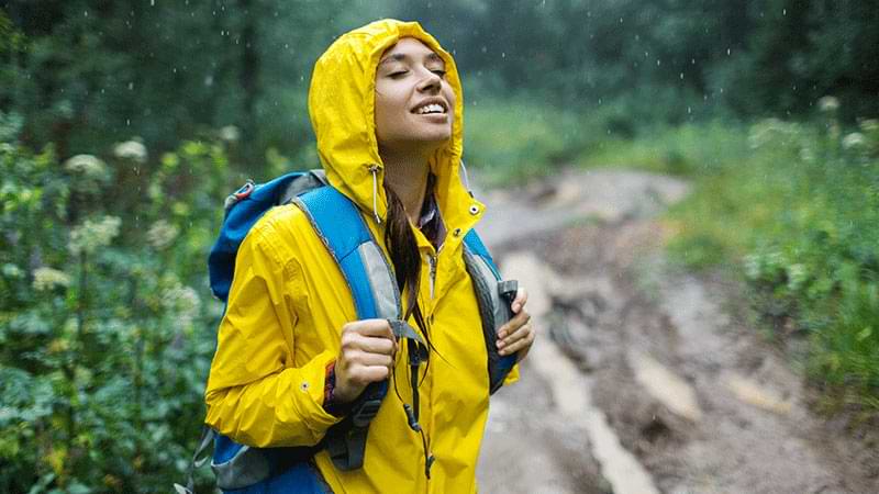Mujer joven con impermeable disfruta de la naturaleza bajo la lluvia