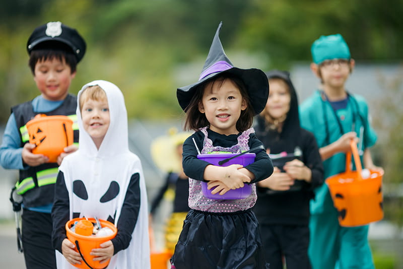 group of children in Halloween costumes, carrying candy buckets, walking together outside