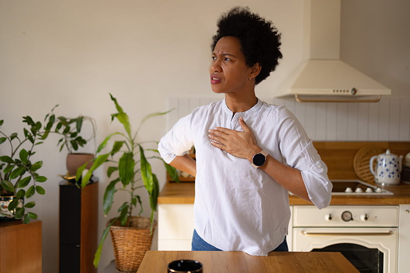 a woman is standing in her kitchen holding her hand over her chest and looking concerned