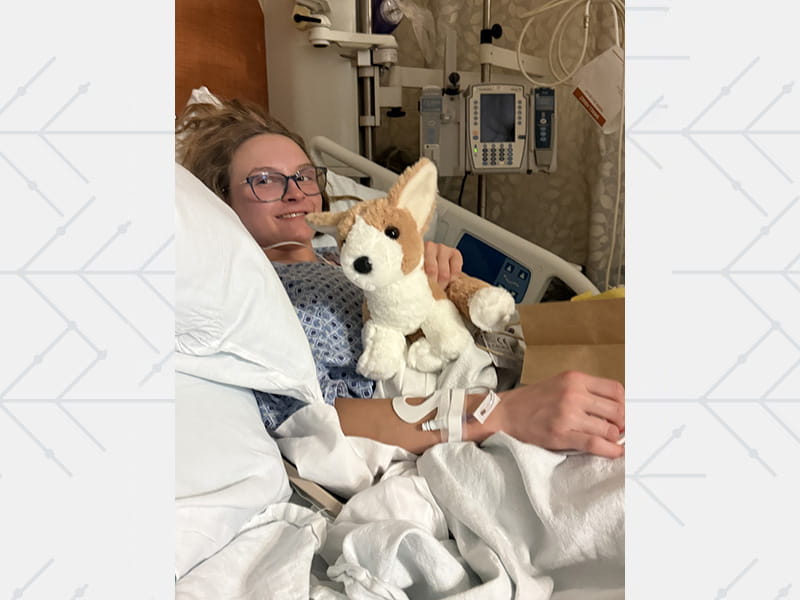 Ryan Haselden, with her stuffed corgi Charlie, in hospital after experiencing cardiac arrest during an event in February 2025