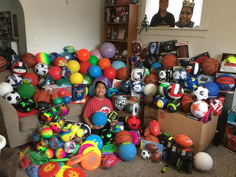 Manny Rios in a living room filled with sports balls for schools in need in 2022
