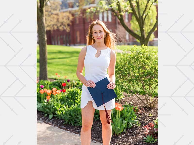 Liv Pines posing with college graduation cap with campus in the background