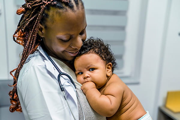 A smiling healthcare professional looking down at an infant cuddled in her arms