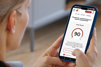 Close up looking over a woman's shoulder at her phone screen, showing her score on a health assessment on the Heart.org website