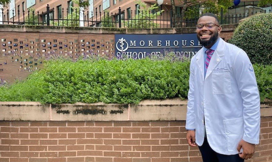 Jalen Robinson is in his lab coat standing in front of the Morehouse School of Medicine campus sign.