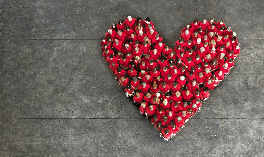 An aerial view of a crowd of people wearing red, forming a heart shape.