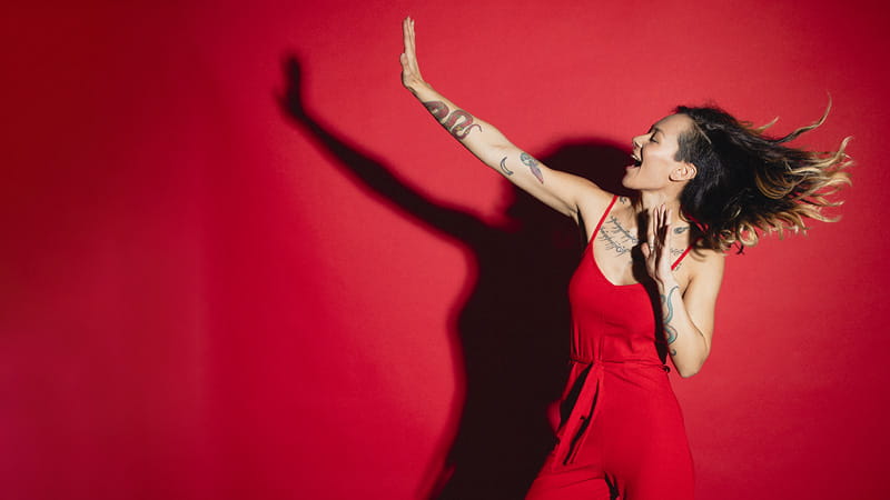 Young tattooed woman in a red jumpsuit dancing in front of a red background