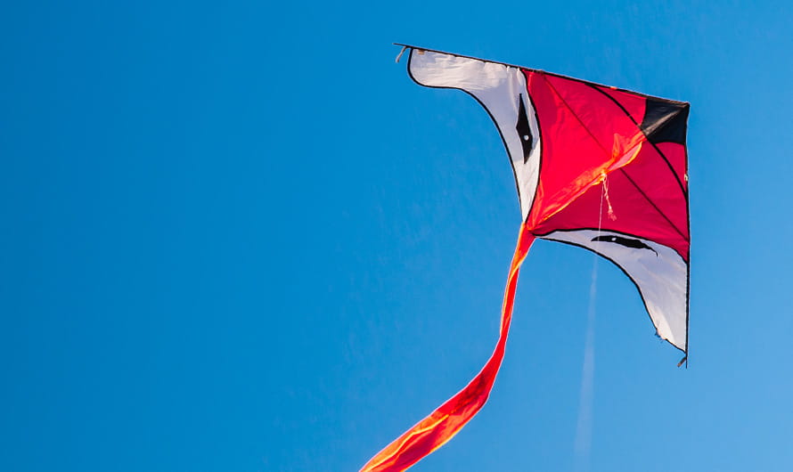 Looking up at red and white kite flying against a blue sky
