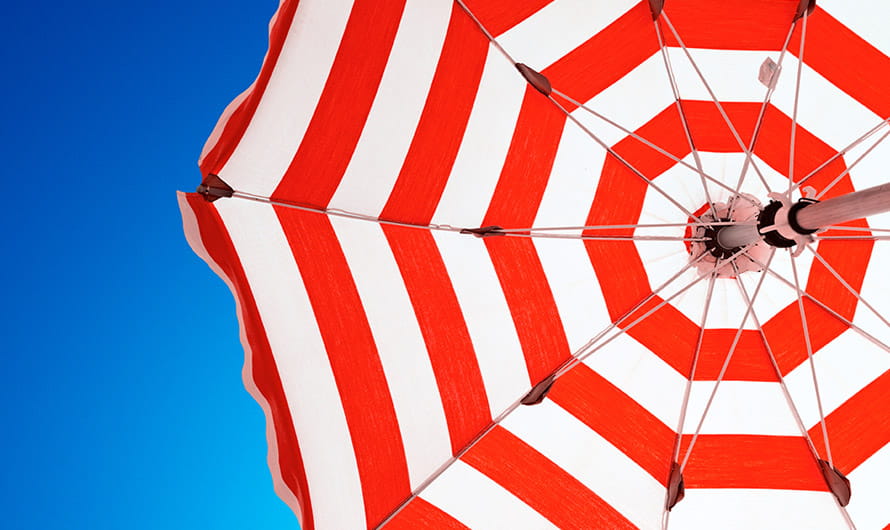 Looking up from under an open red and white striped beach umbrella against a blue sky