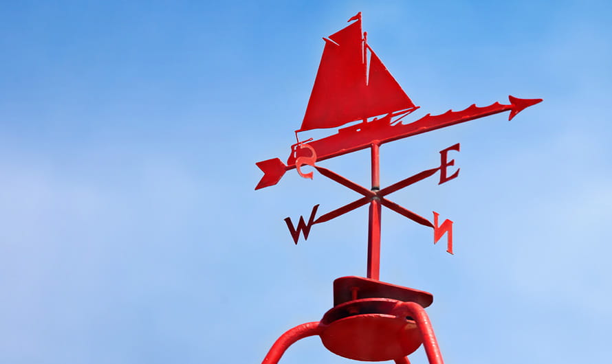 A red sailboat weather vane against a blue sky
