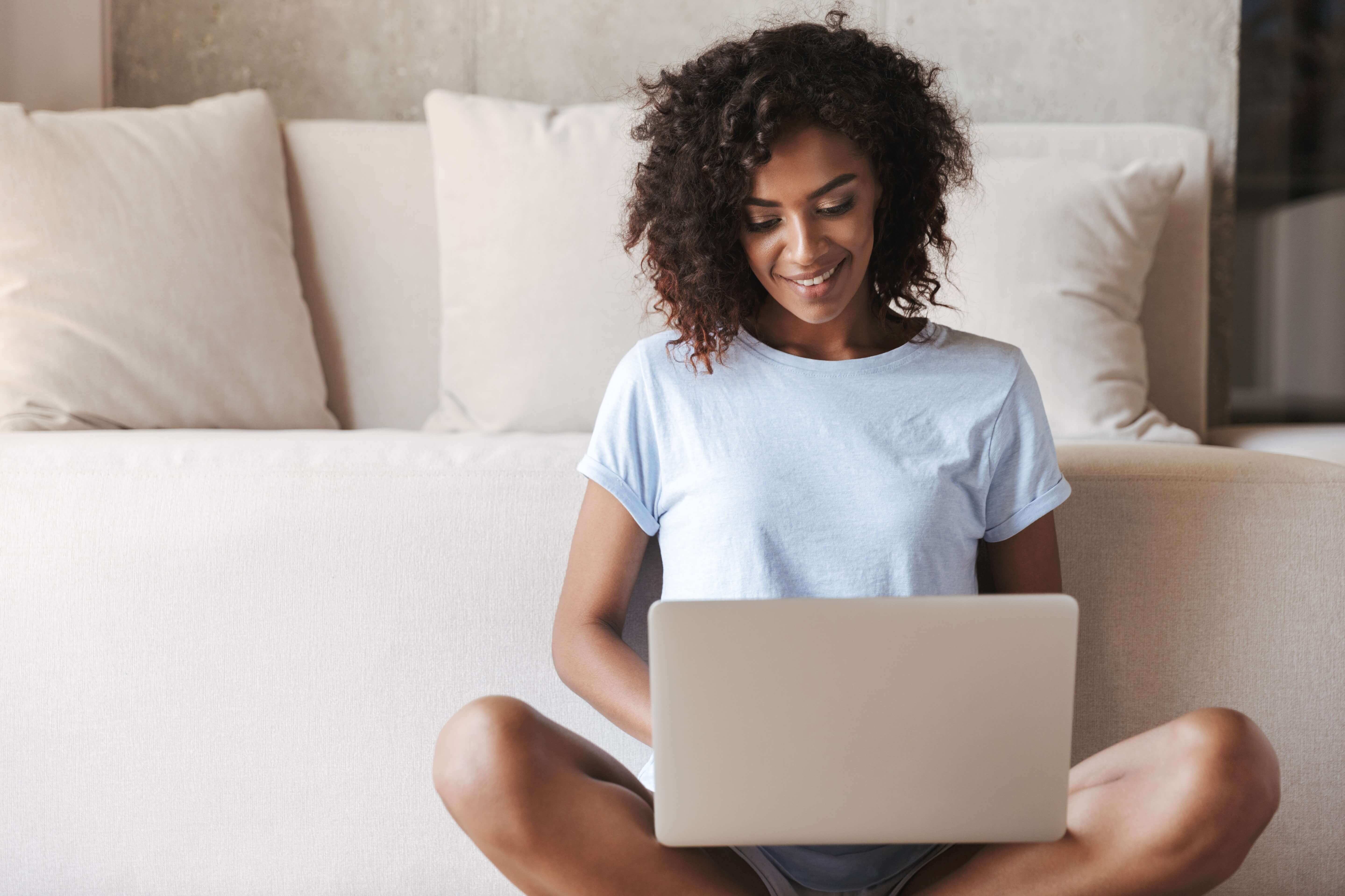 Smiling woman sits on floor with computer in lap