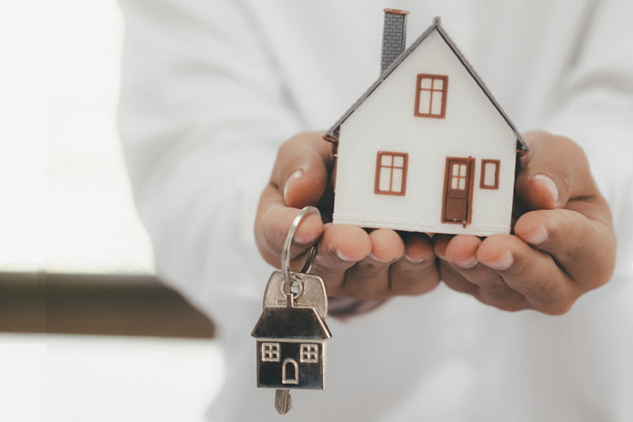 Hands holding out a model house and a keyring with key attached