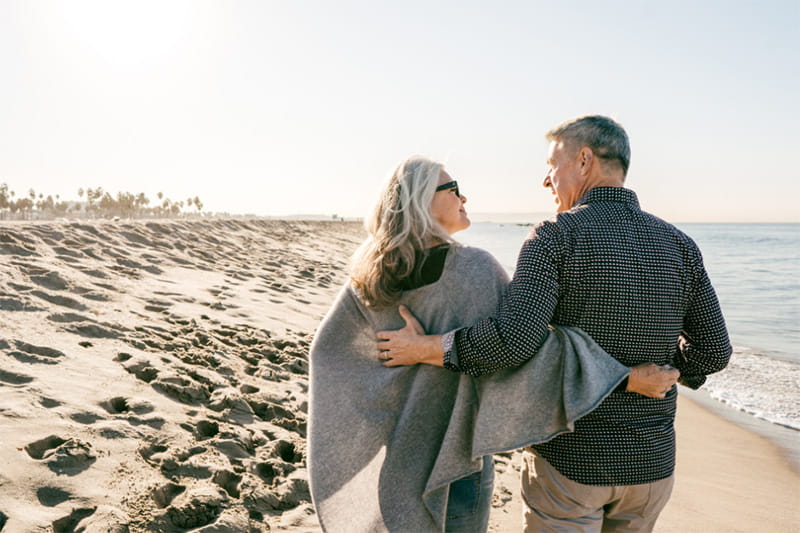 Retired couple walking with arms around each other on a sandy beach