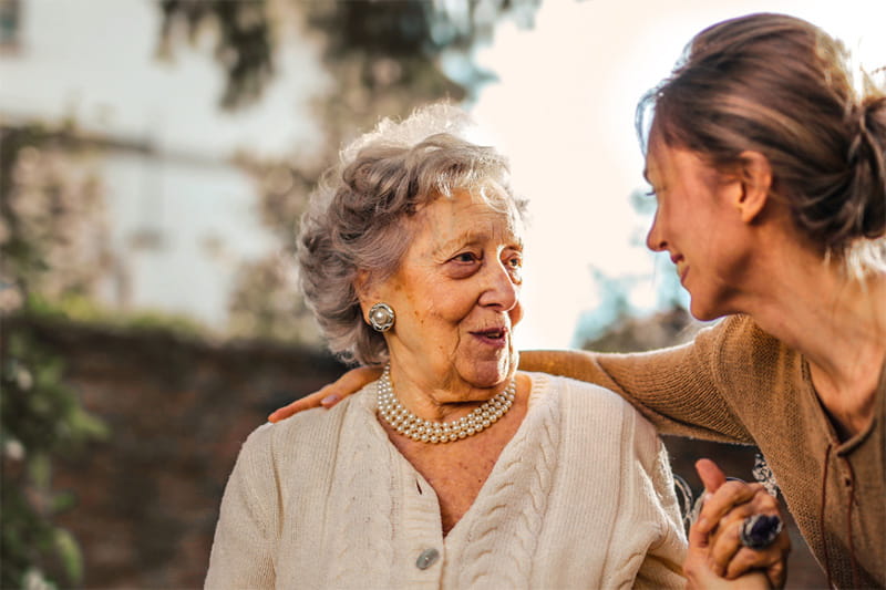 Elderly mother with adult daughter smiling and talking outside