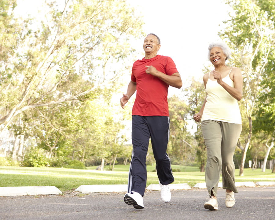 Older black couple jogging together outside on a sunny day