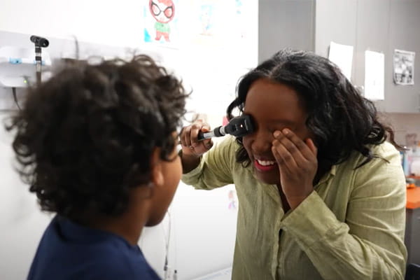 A doctor with Strong Children Wellness is assessing a young patient's eyesight in an examination room.