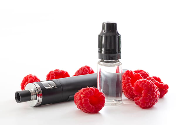 Display of raspberries surrounding a vape and vape juice in a bottle