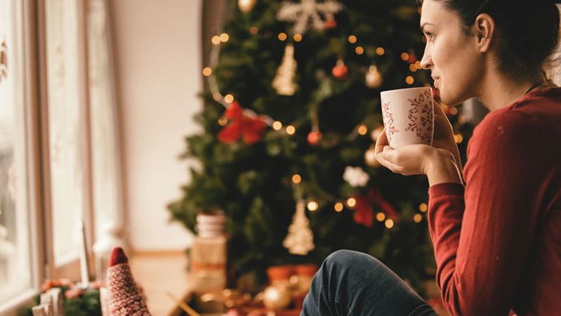 Mujer joven bebiendo té al lado del árbol de Navidad.