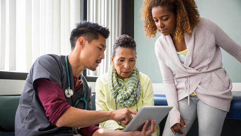 healthcare provider consulting with senior female patient and adult daughter in exam room