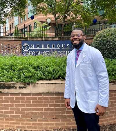 Jalen Robinson is in his lab coat standing in front of the Morehouse School of Medicine campus sign.