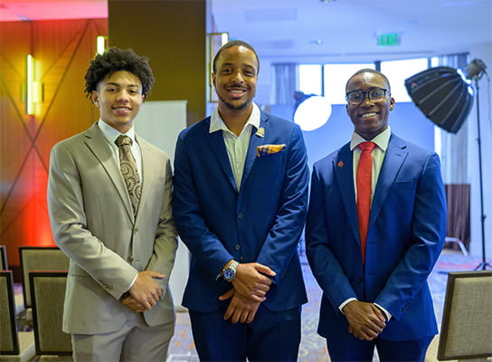Two American Heart Association Scholars in suit and tie posing with a program alumni.