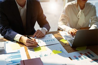 View of top of a desk, where a man and a woman in business attire are reviewing documents and charts