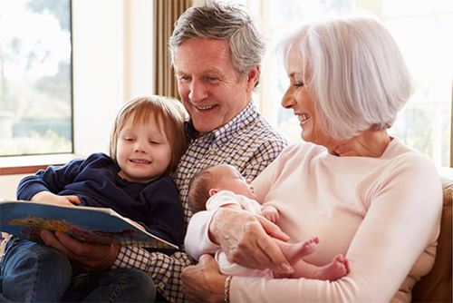 grandparents holding their grandchildren and reading a story book to them