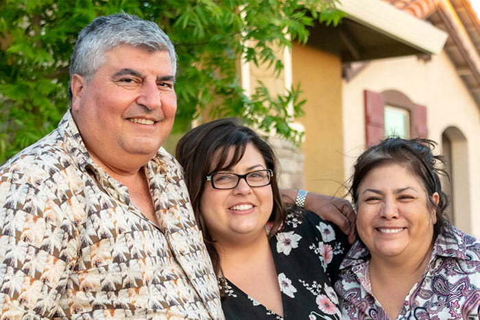 group of three adults smiling and standing close together outdoors