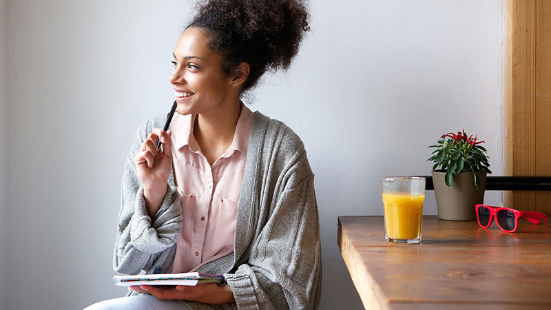 mujer afroamericana en piyama sonriendo mientras escribe su diario