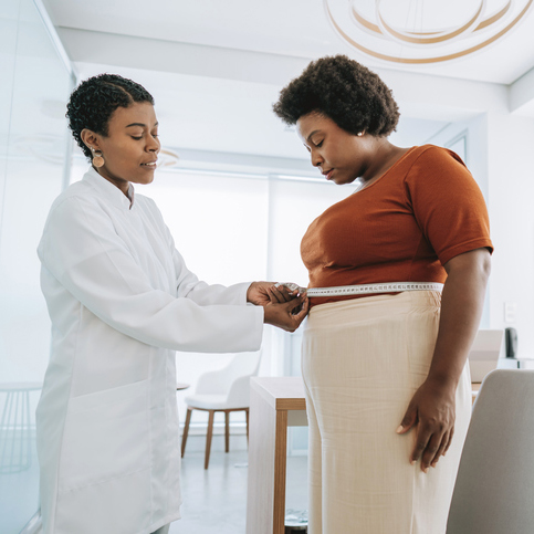 A female doctor helps to measure a woman patient's waist to check progress