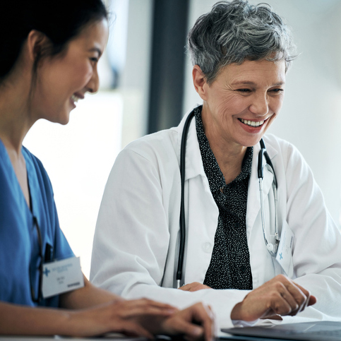 A doctor and a nurse are smiling looking at a laptop together