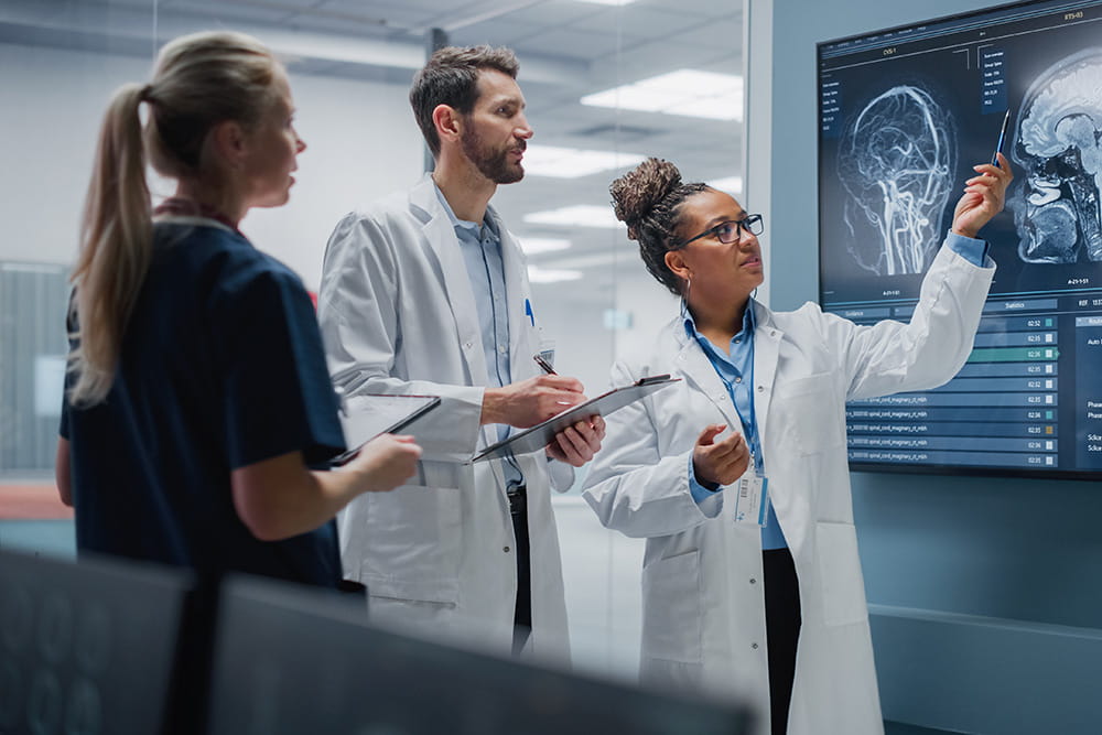 Three health care professionals reviewing diagrams on large screen and taking notes