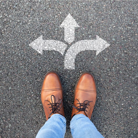 close up of a person's feet in loafers standing in front of a symbol of arrows pointing in different directions on the pavement